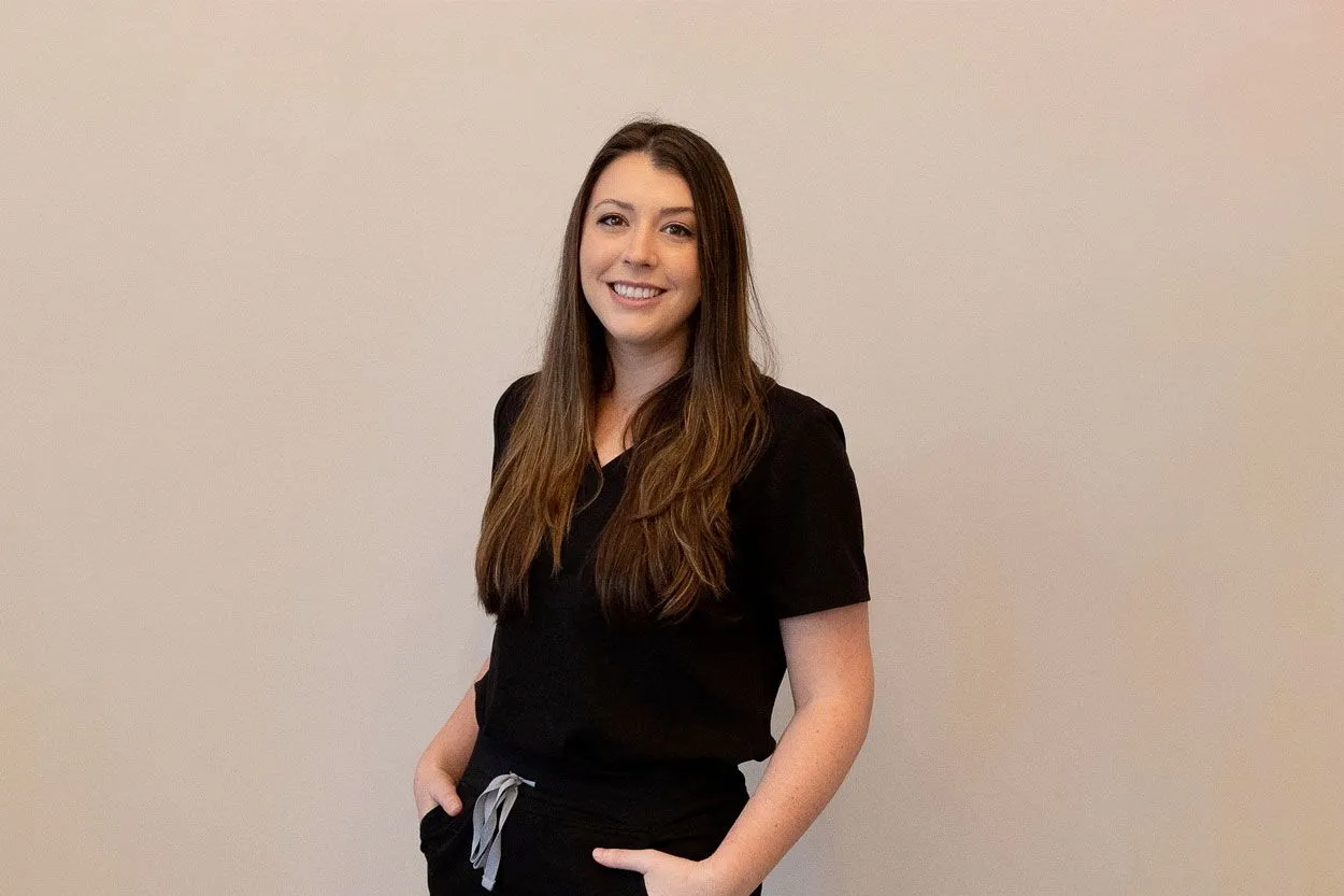 Photo of Sarah from Liv Aesthetics LLC, smiling confidently in a black uniform. She stands against a softly lit background, reflecting a warm and professional presence.