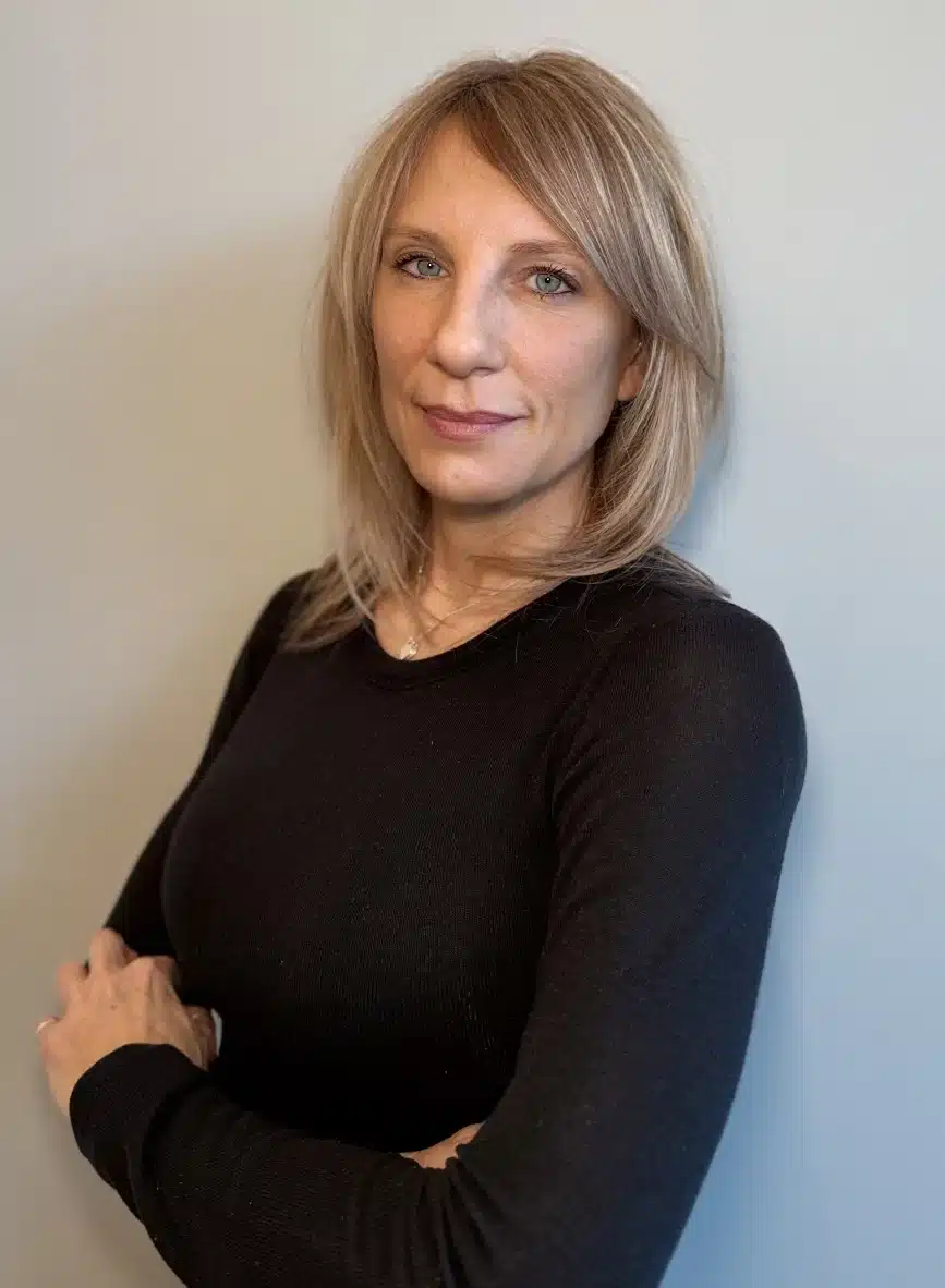 Photo of Dianne from Liv Aesthetics LLC, smiling confidently in a black top. She stands before a neutral-toned background, presenting a welcoming and professional presence.