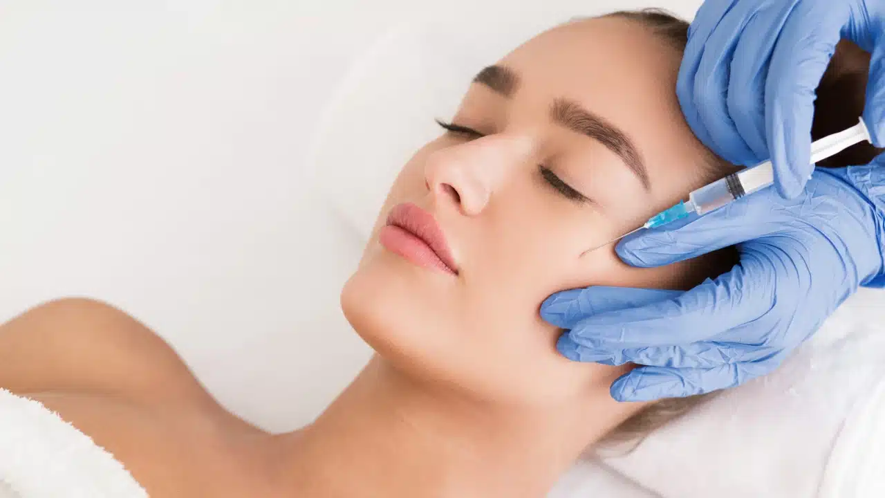 Close-up image of a Radiesse dermal filler injection being administered to the lower face. A gloved professional carefully treats the area to enhance volume and smooth deep lines.