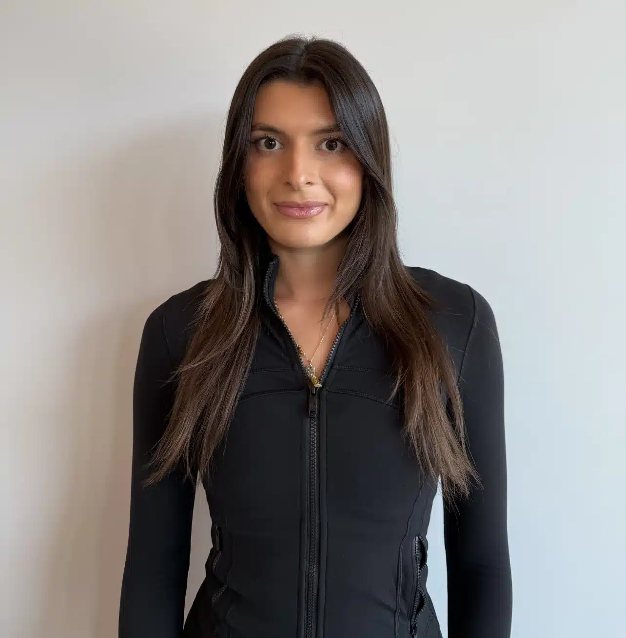 Photo of Sophia from Liv Aesthetics LLC, smiling warmly while wearing a black top. She stands against a softly lit background, conveying professionalism and approachability.